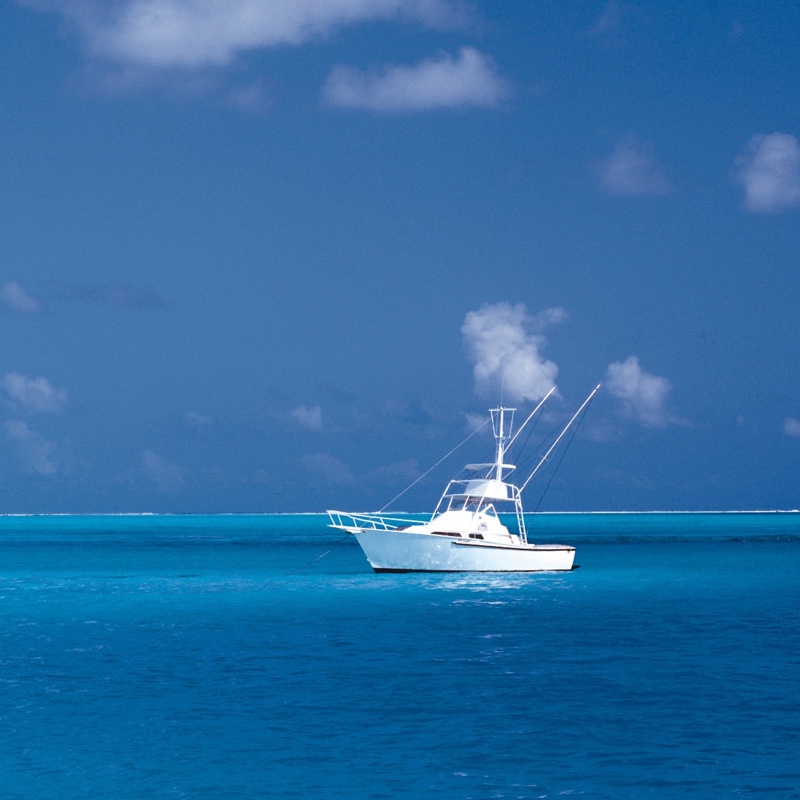 Far shot of smaller white yacht boat on crystal blue waters